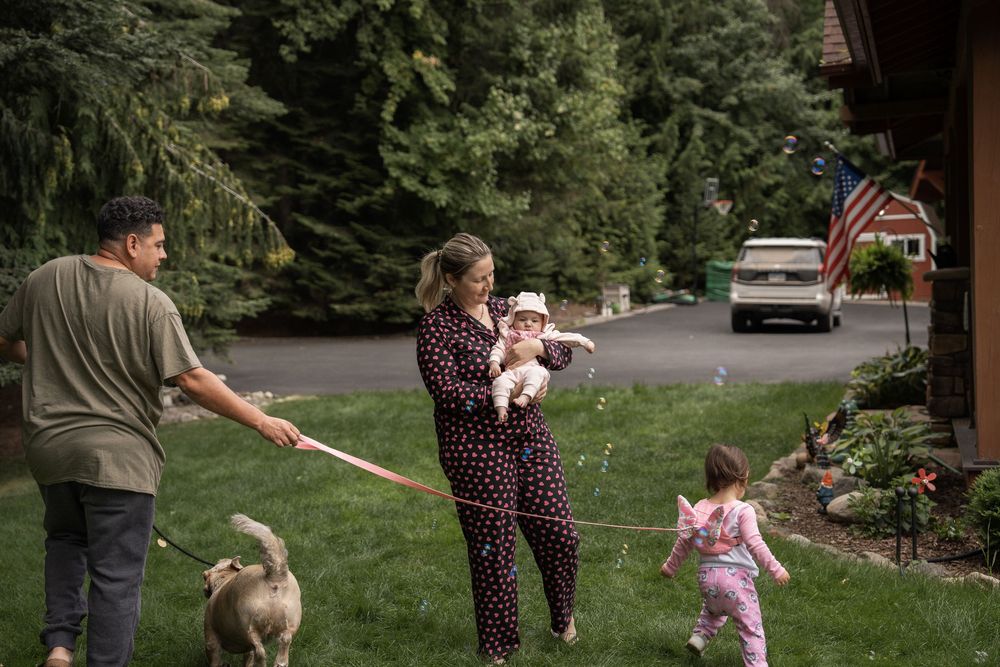 A family plays together on a grassy slope near a house with trees in the background.