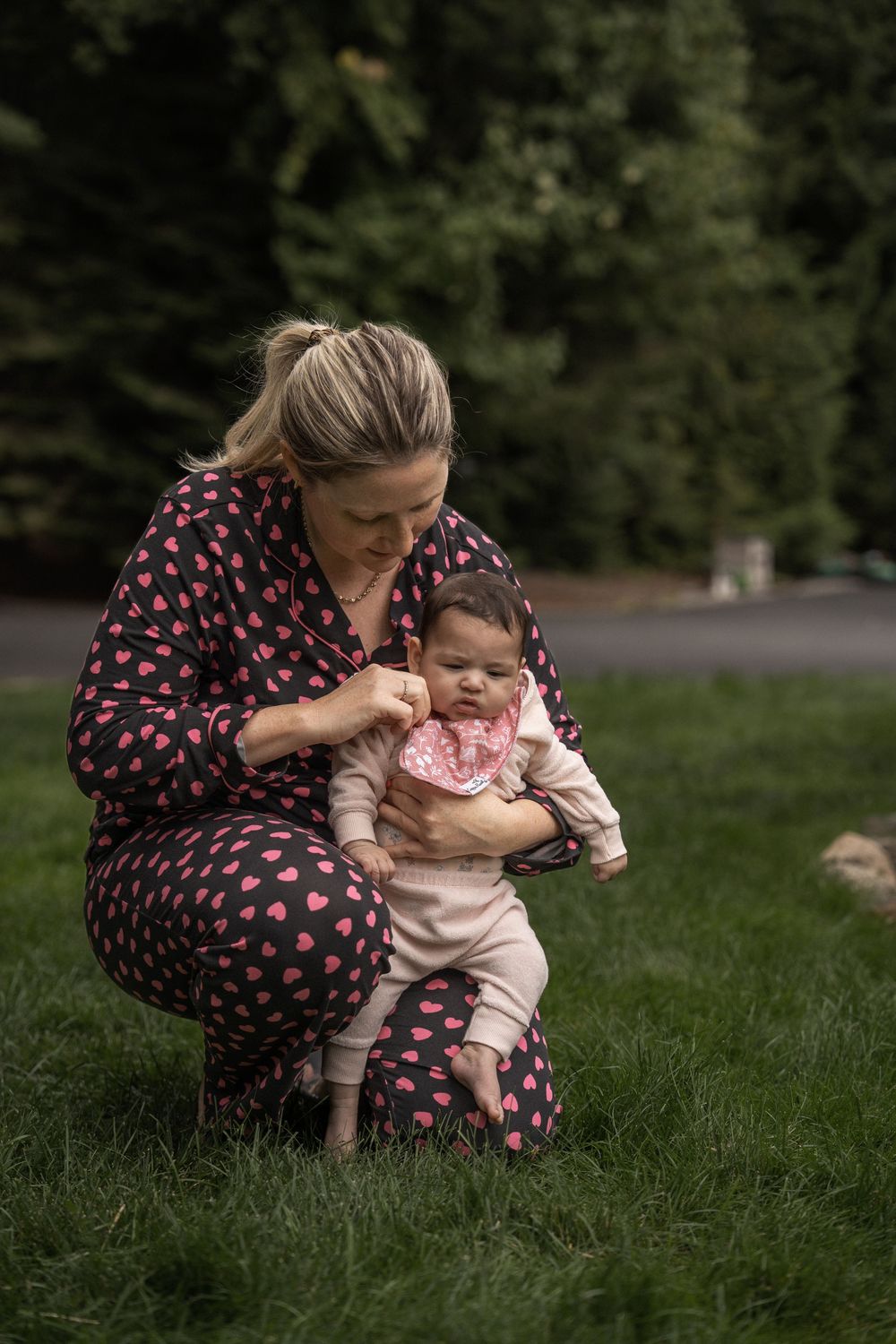 Parent and baby share tender moments while sitting together on grass in a park setting.