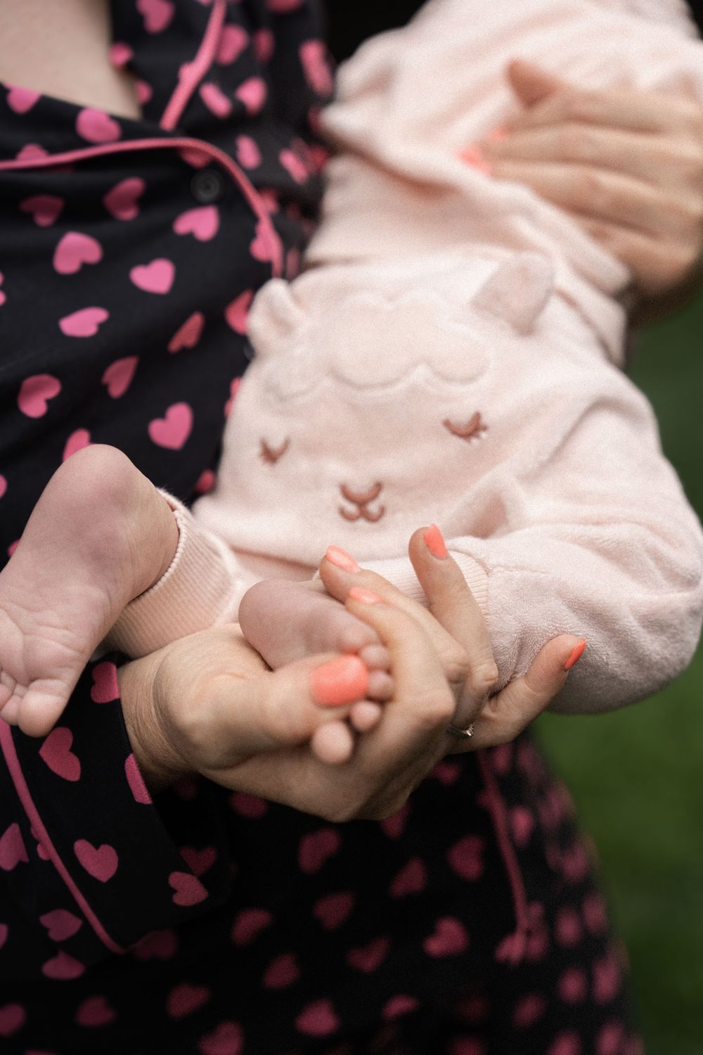 Close-up of tiny baby feet being gently held against a pink sleeve and black dress with heart pattern.