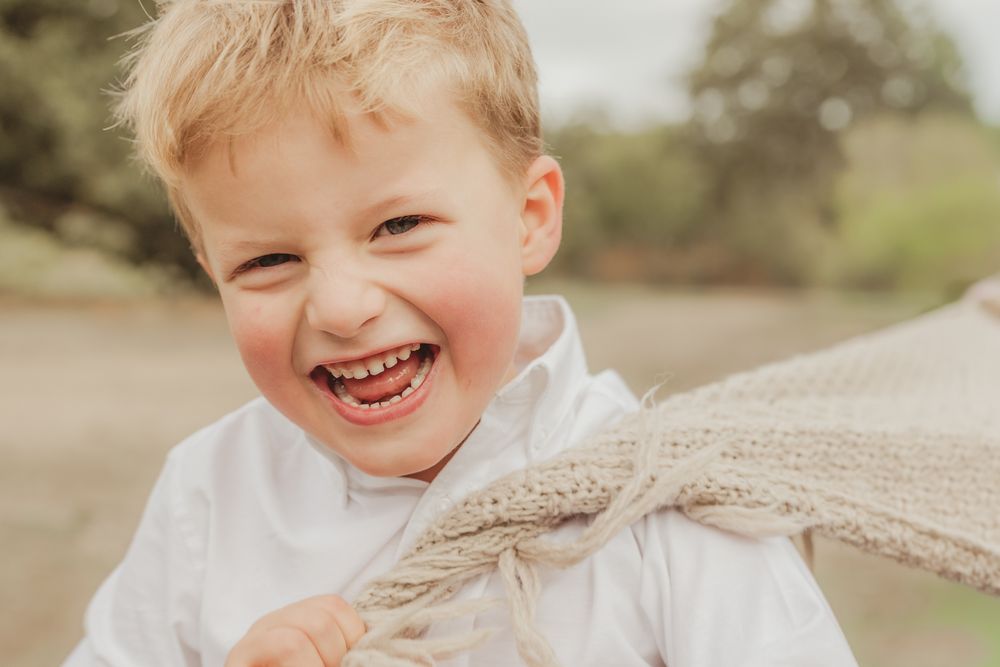 A joyful child in a white shirt laughs while holding a large wheat stalk in a sunny outdoor setting.