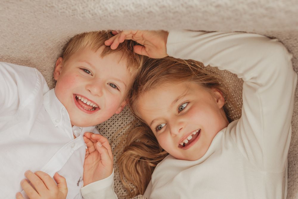 Children lying together on white bedding with soft warm lighting creating a cozy atmosphere.