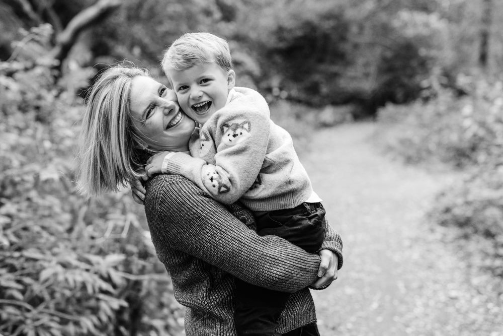 A series of black and white candid family moments captured on a wooded path showing affectionate embraces and laughter.