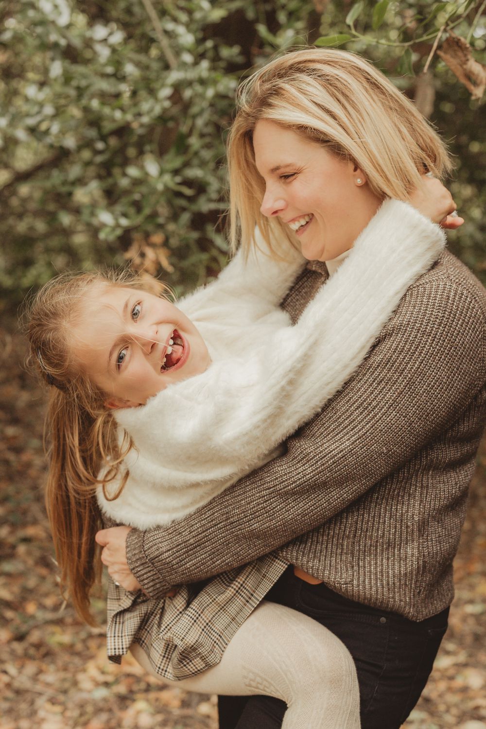 A parent and child share a joyful embrace while wearing cozy sweaters in an autumn outdoor setting.