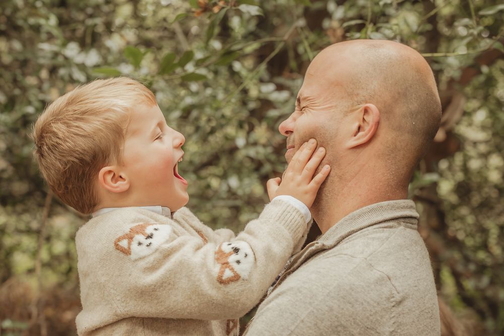 A tender moment captured between parent and child during a playful outdoor photoshoot in a natural setting.