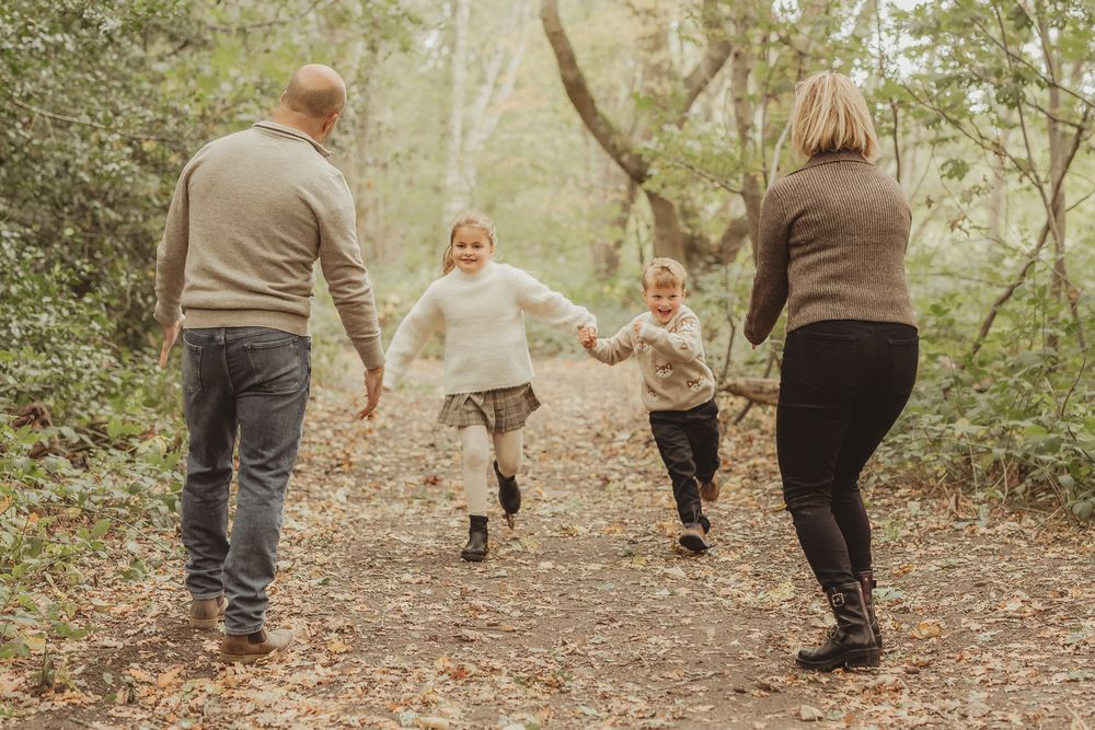A family holds hands while walking together through a wooded trail on an autumn day.