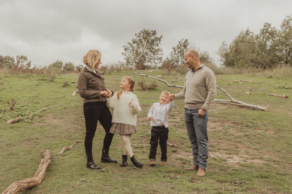 A family of four enjoying a casual moment together on a grassy hillside during an overcast day.