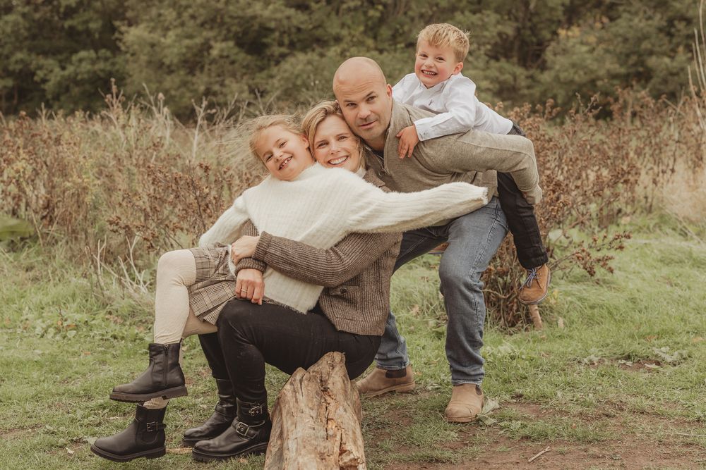 A playful group poses together on a tree stump in a natural outdoor setting with tall grass and greenery.