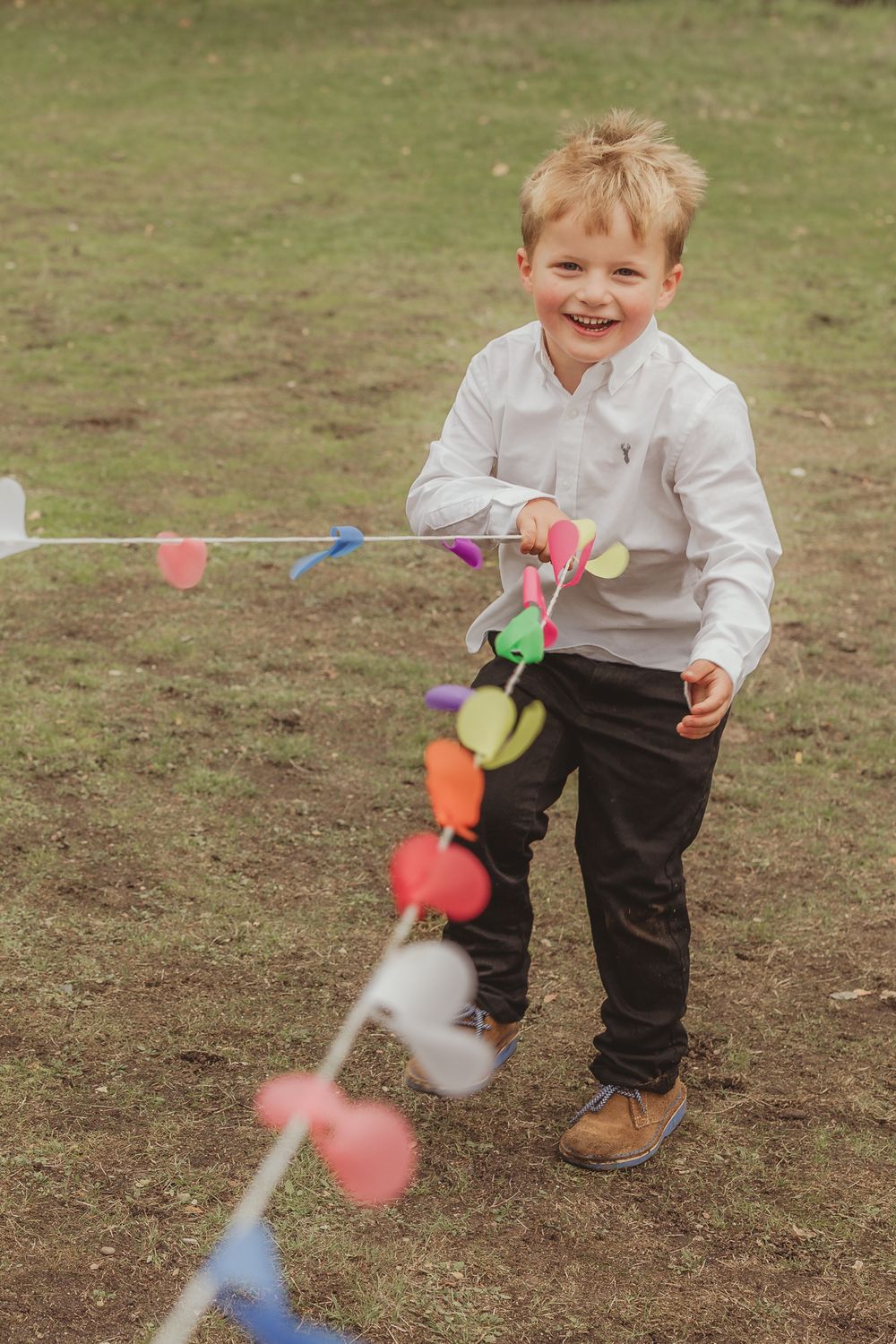 A child in a white shirt plays with colorful paper airplanes on a grassy field.