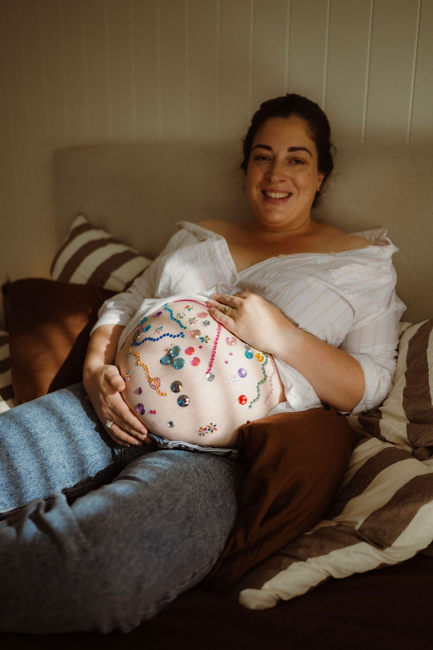 Smiling pregnant woman reclining on bed with colorful belly art painted on her baby bump.