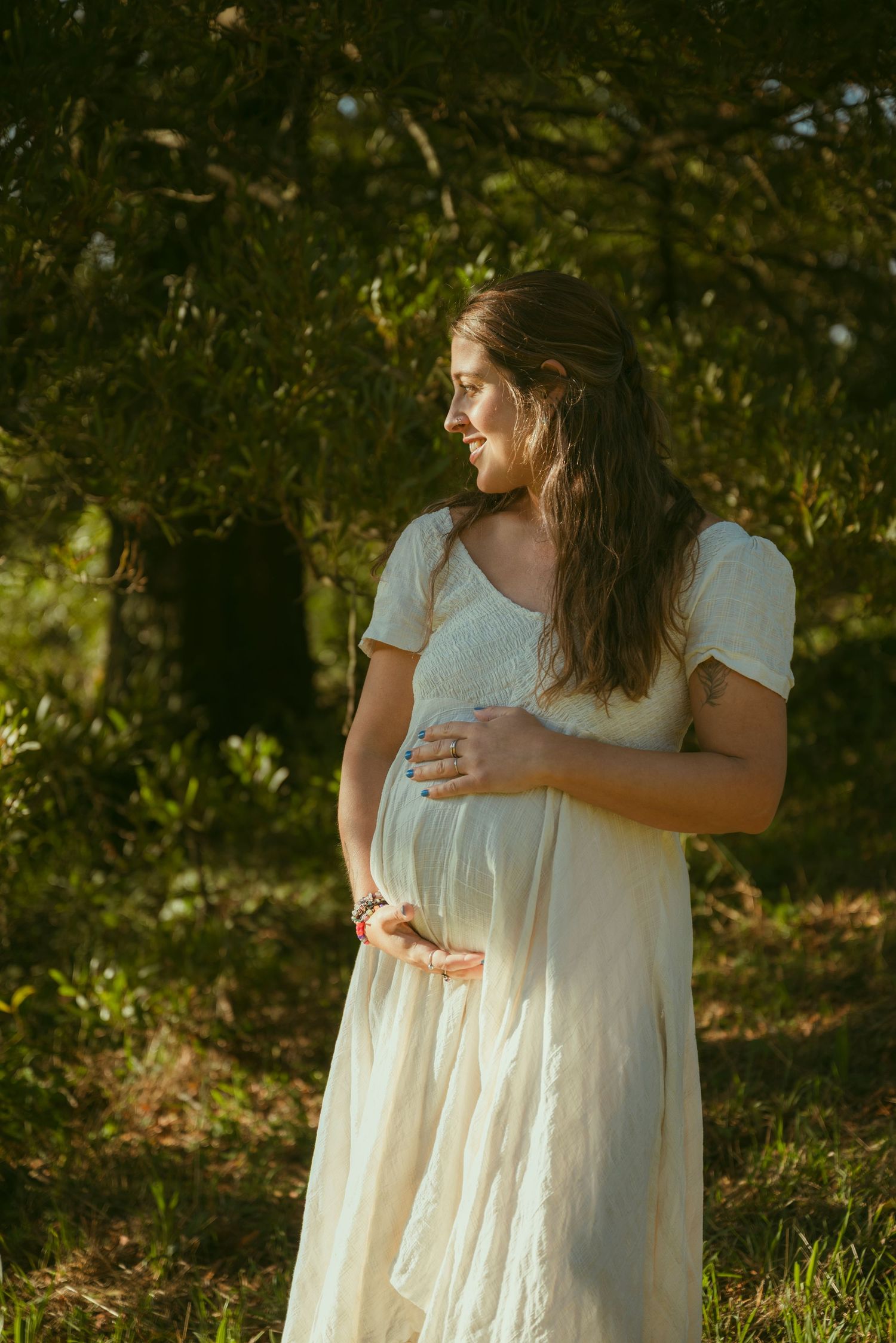 Person in pink dress sitting on large rock in wooded forest setting.