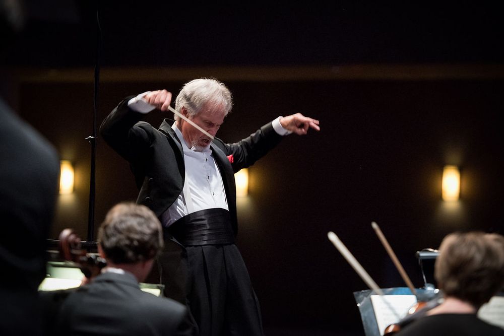 Orchestra conductor in formal attire passionately directing a symphony orchestra performance on stage.