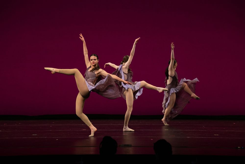 Three female dancers perform synchronized contemporary dance on stage with a pink backdrop.Best photographer Williamsburg VA
