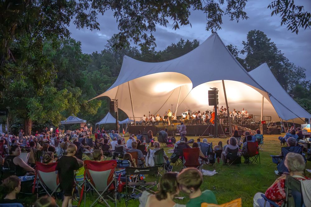 Outdoor evening concert white stretch tents with crowd seated on lawn chairs surrounded by trees. Best photographer Williamsburg VA