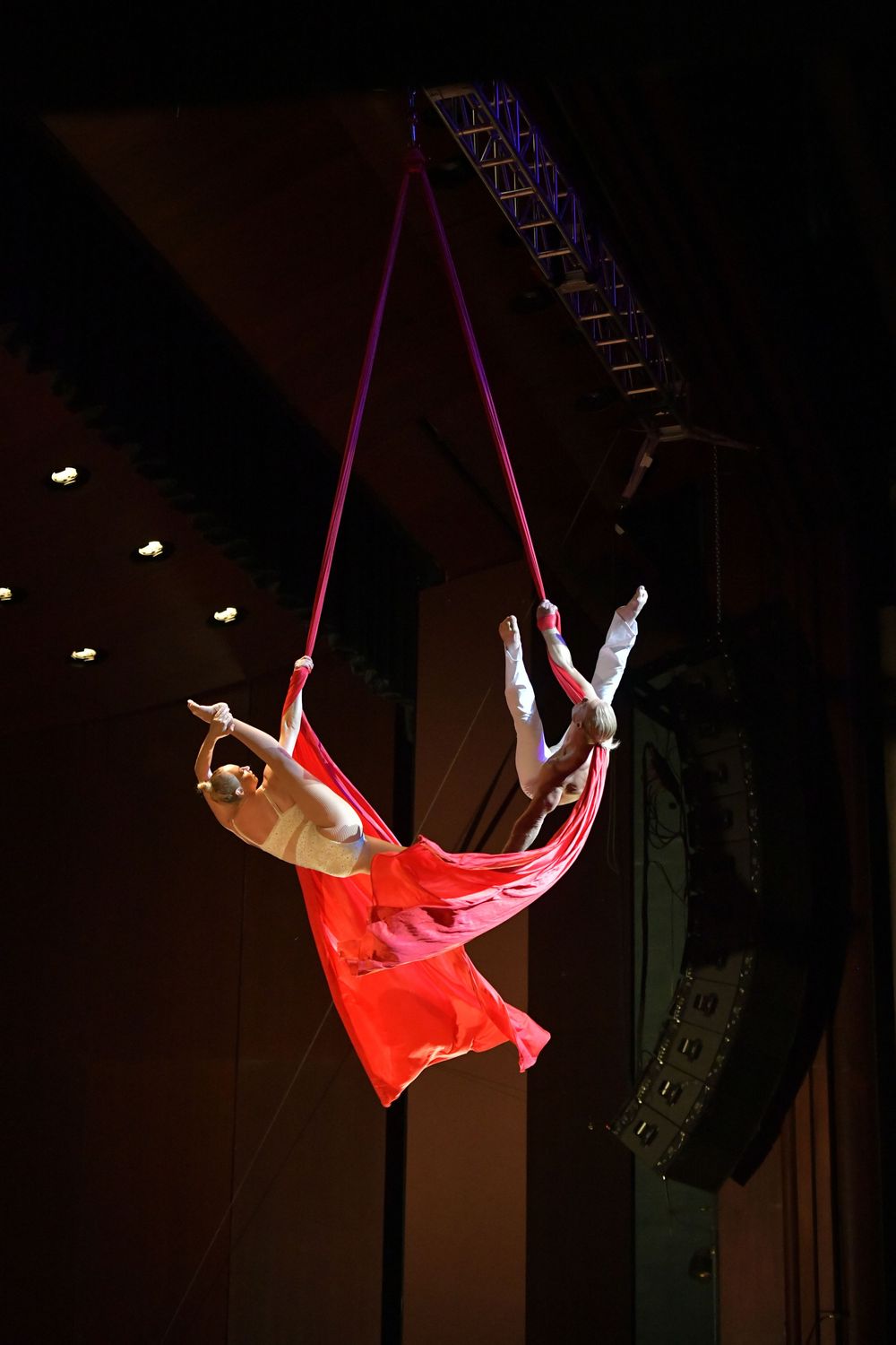 Two acrobats perform aerial silk routine, suspended mid-air in red fabric under stage lighting.Best photographer Williamsburg VA