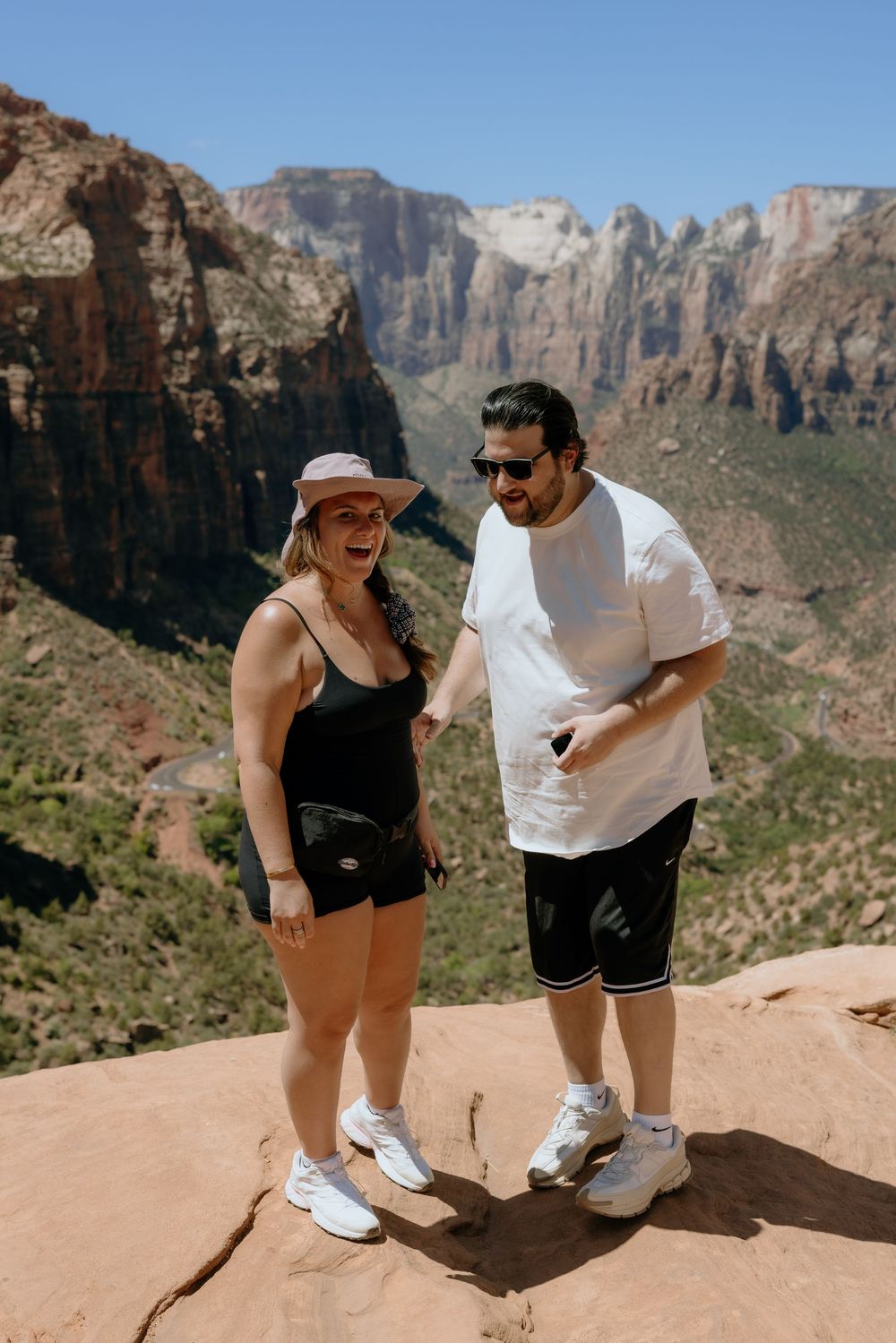 A couple enjoys a scenic view while hiking on a red rock trail overlooking a canyon landscape in the mountains.