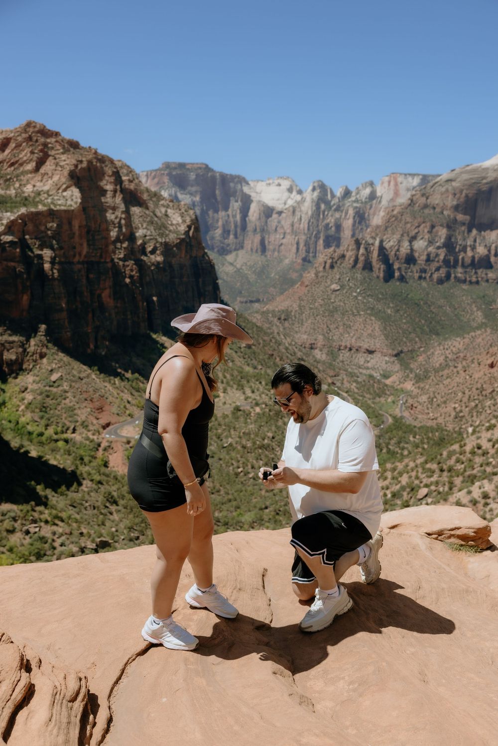 A couple shares a special moment during a proposal on a scenic overlook at Zion National Park with towering cliffs behind them.