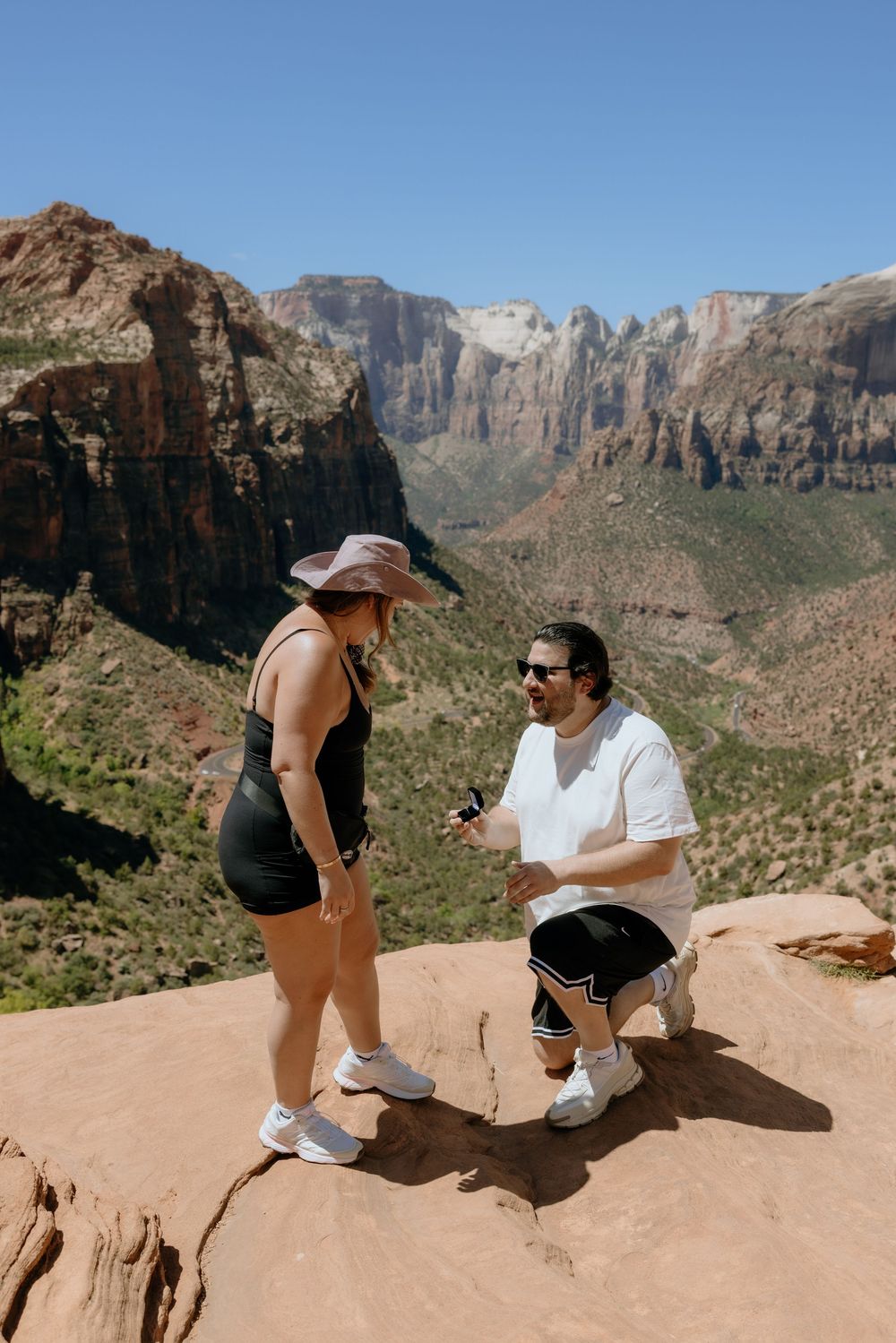 A couple sits on a rocky ledge overlooking the dramatic canyon landscape at Zion National Park.