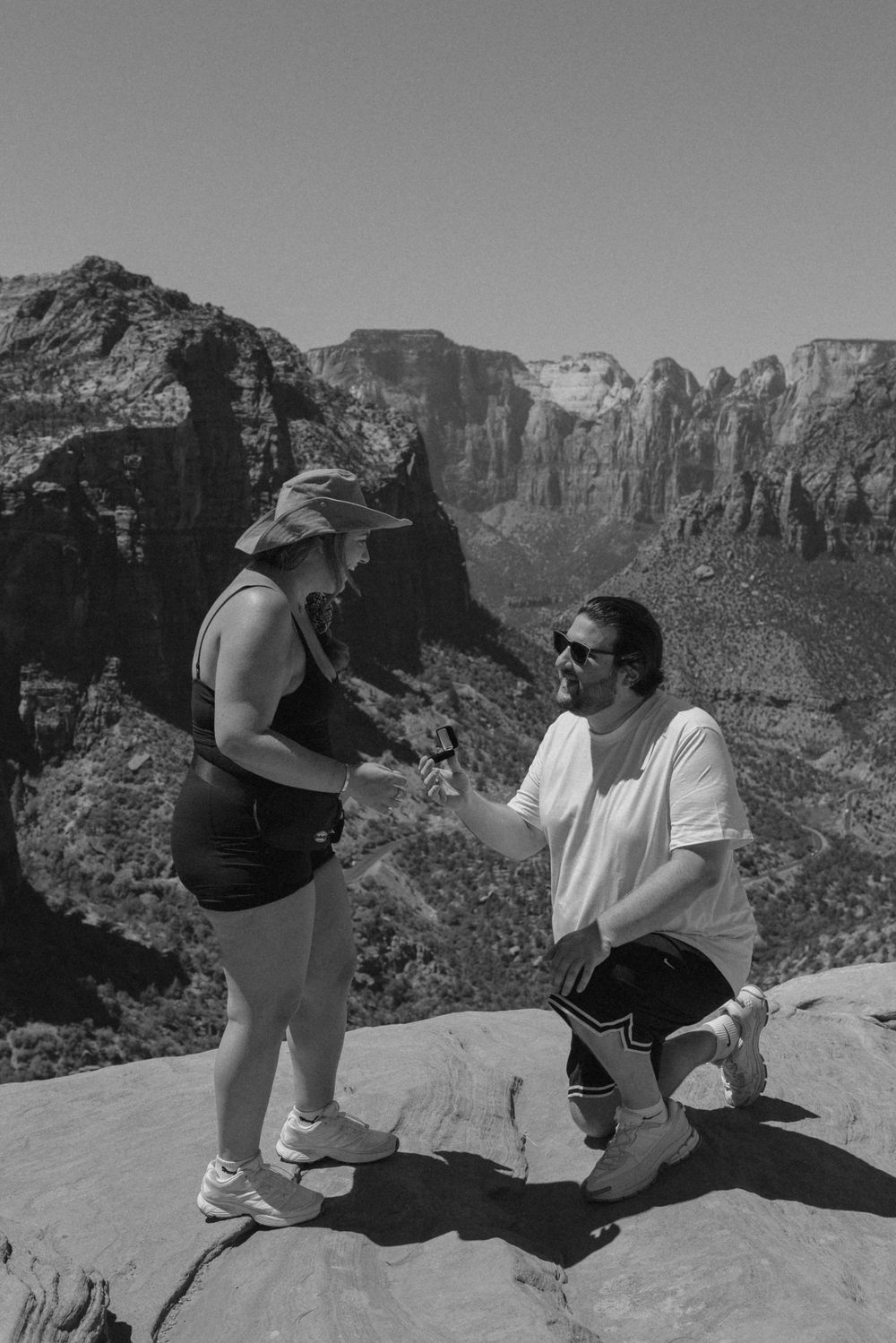 Hikers rest on a cliff edge overlooking a vast canyon landscape with towering rock formations.
