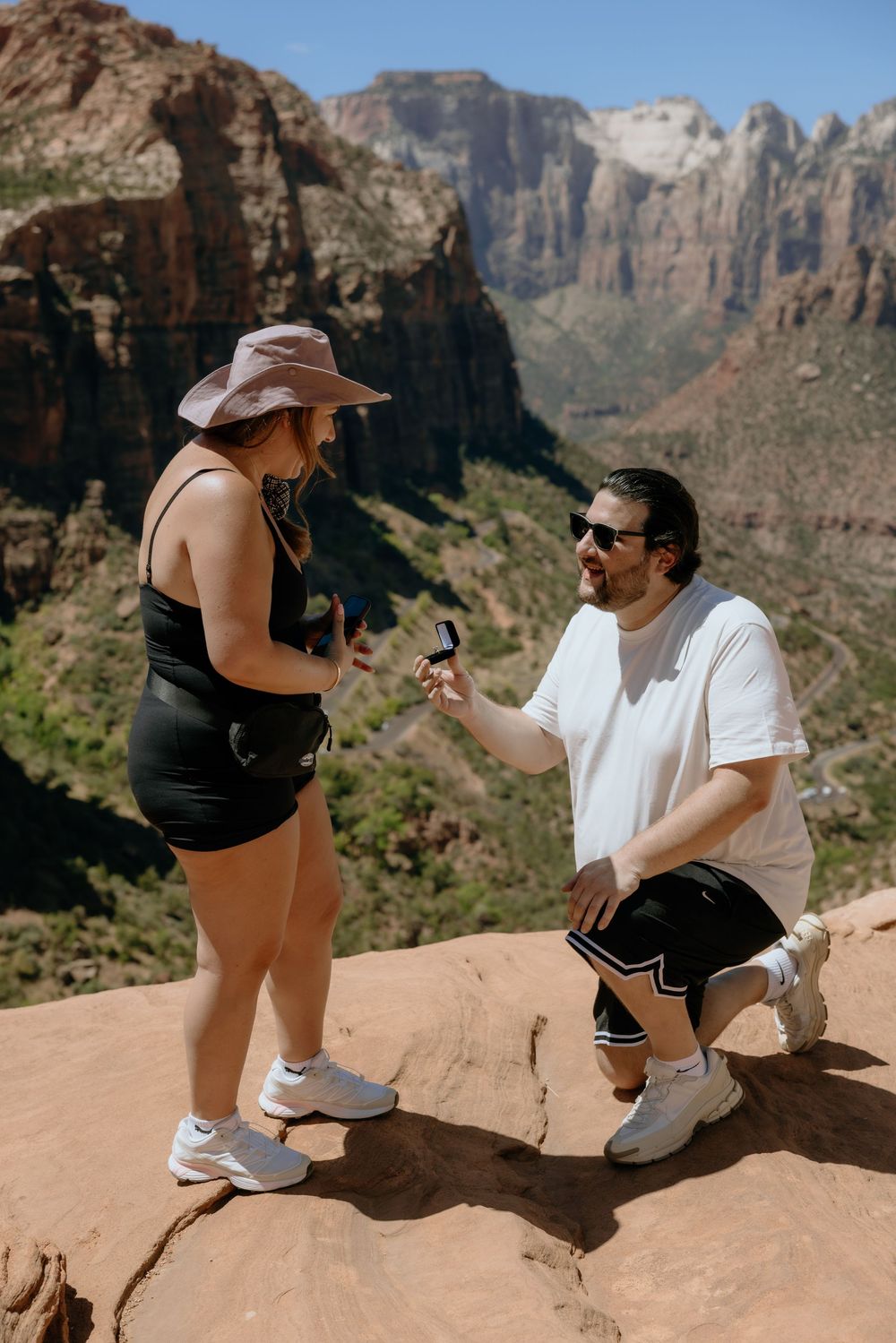 A couple sits on a rocky ledge overlooking the majestic cliffs and canyons of Zion National Park in Utah.