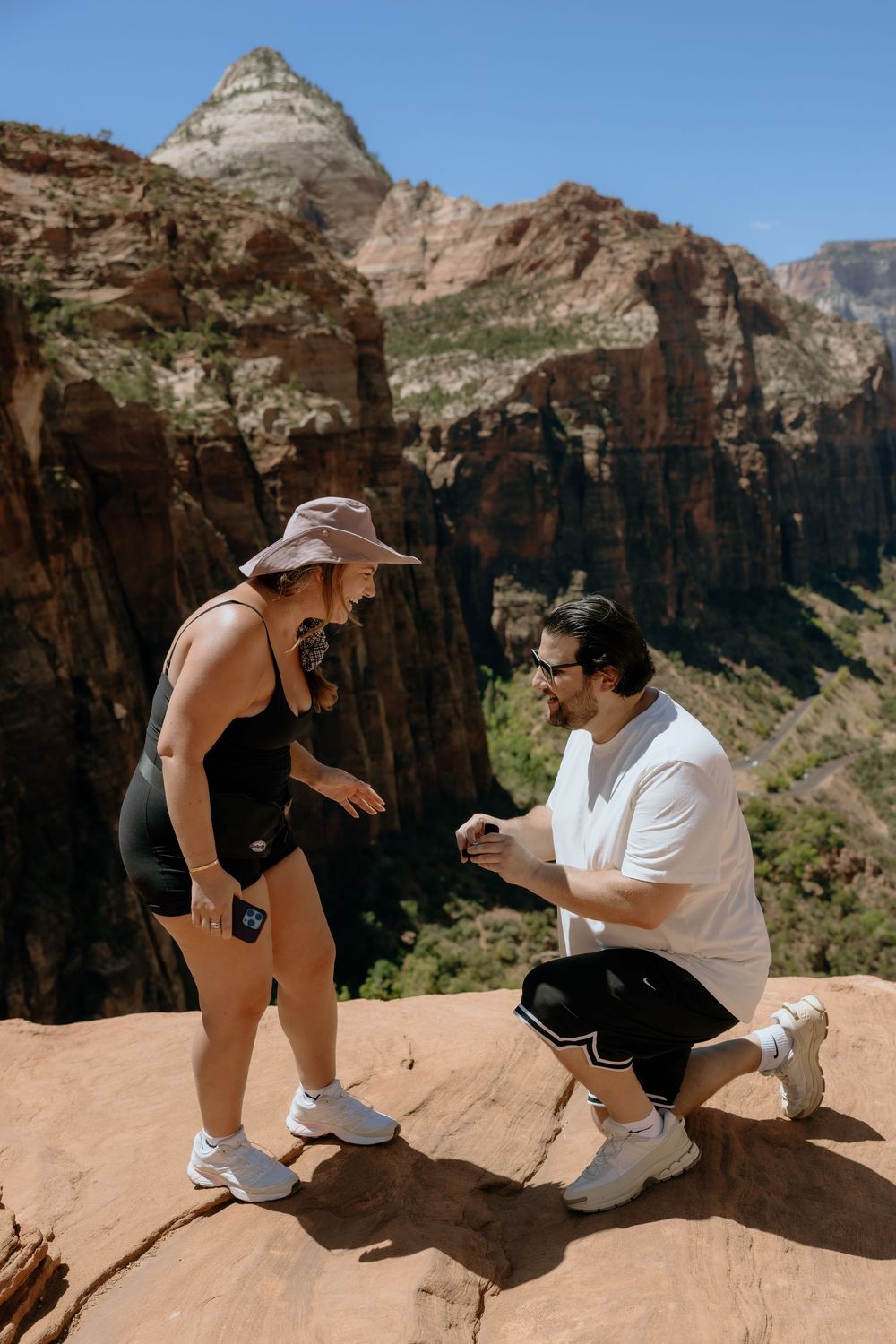 A marriage proposal takes place on a scenic rocky overlook with dramatic canyon cliffs in the background.