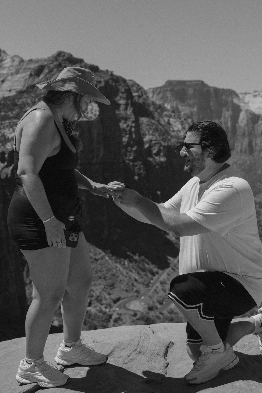 Black and white photo of hikers sharing a lighthearted moment while resting at a scenic mountain viewpoint.