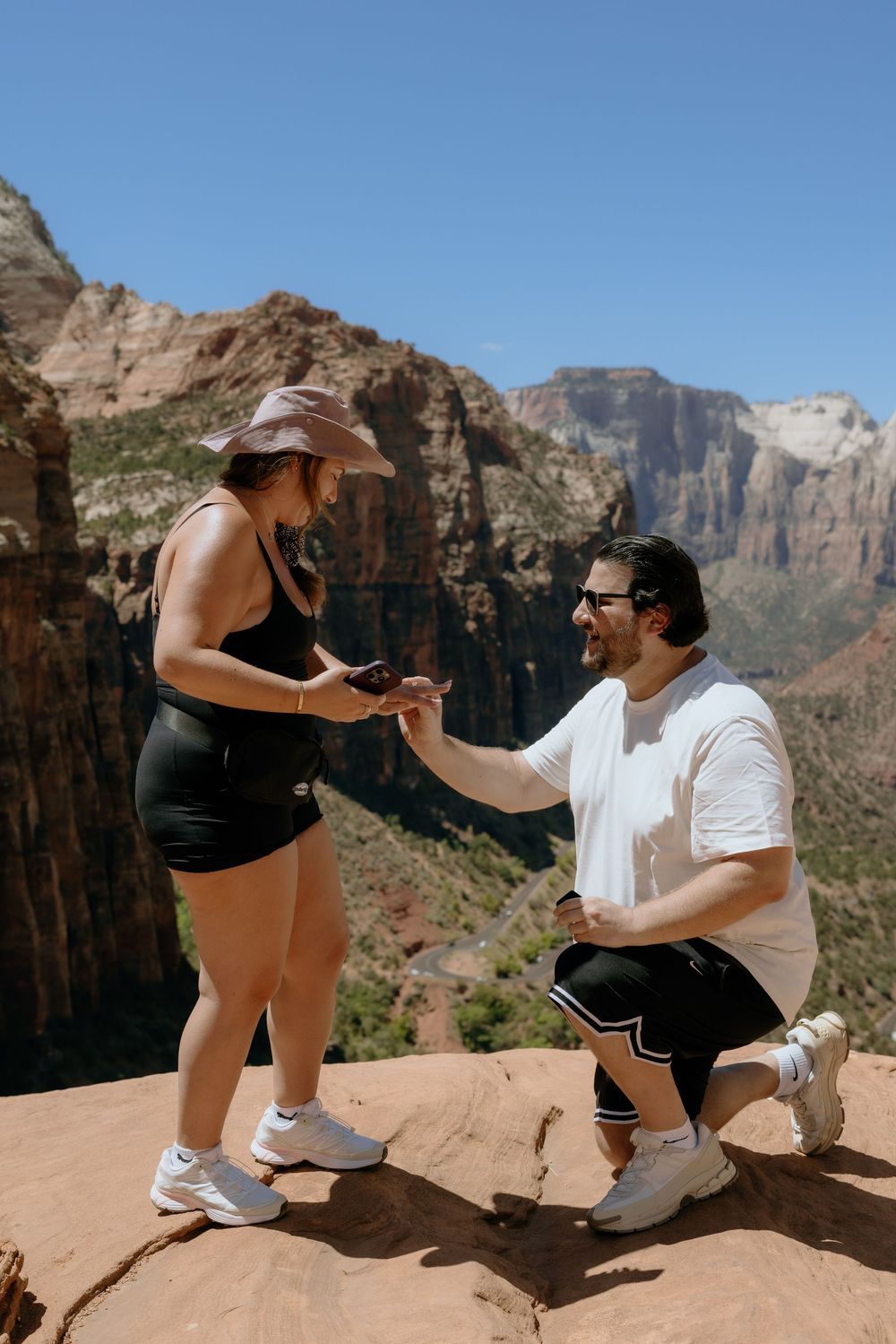 A proposal moment unfolds on a scenic cliff edge at Zion National Park with dramatic canyon views in the background.