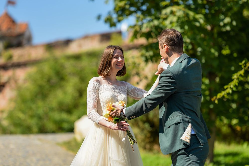 A wedding couple shares a romantic moment in a lush green garden setting while holding a yellow bouquet.