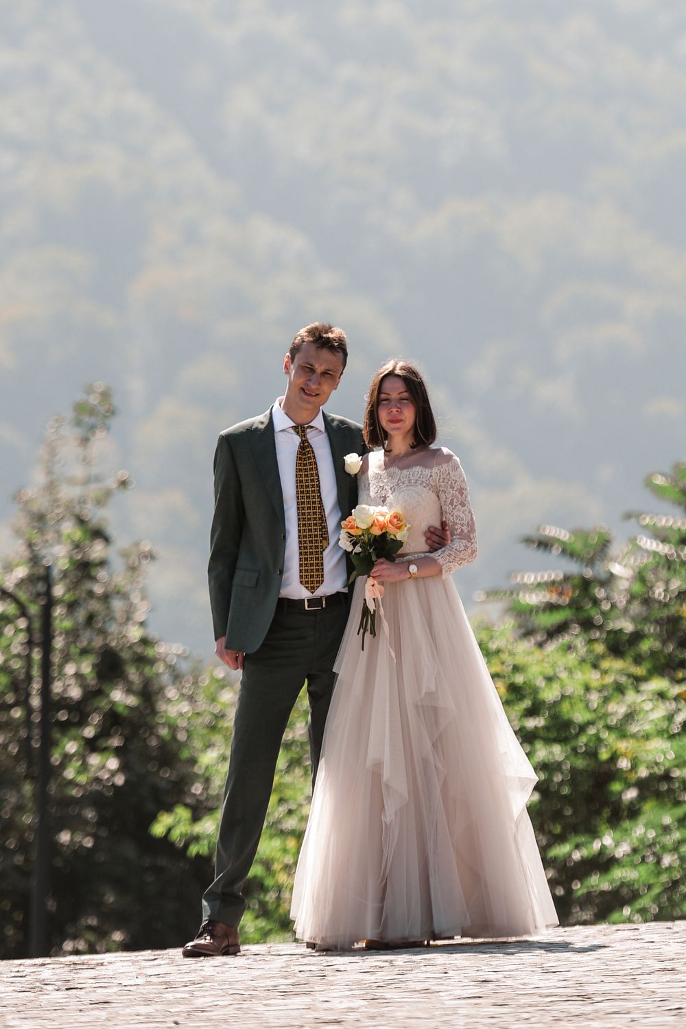 A romantic outdoor wedding scene with a couple posing on a stone wall against a misty mountain backdrop.