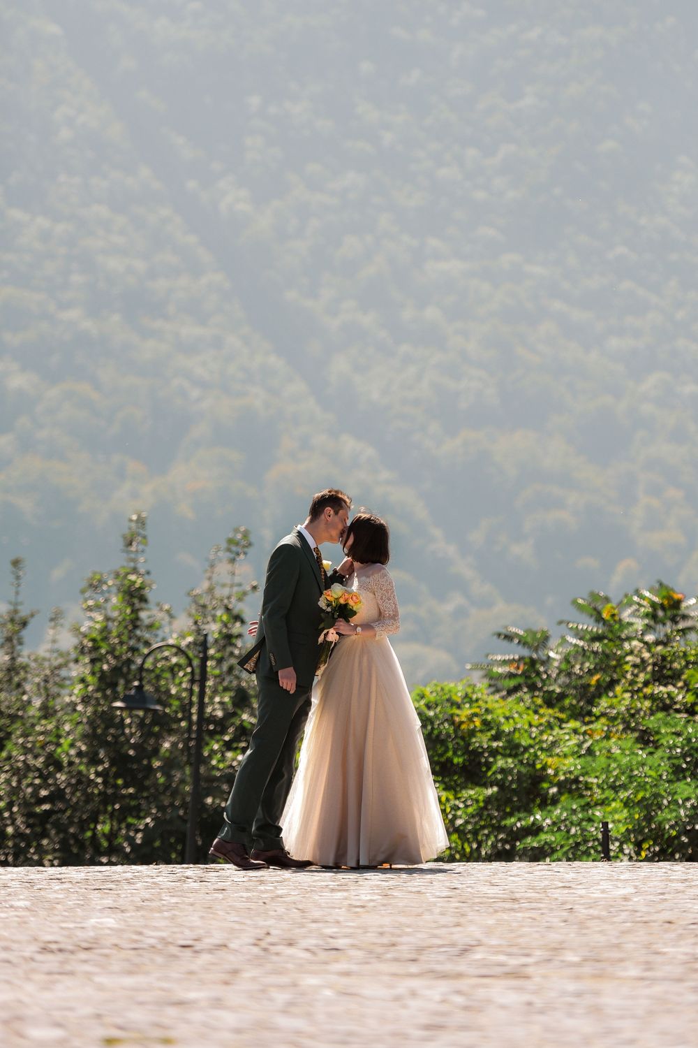 A couple shares a romantic moment on a mountain overlook, with the bride holding yellow flowers against a misty backdrop.