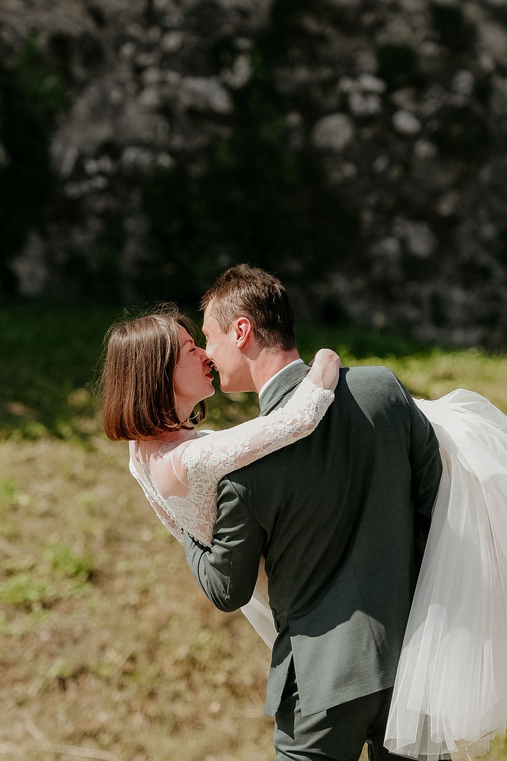 A romantic wedding couple sharing a kiss outdoors while the bride's veil flows in the breeze.