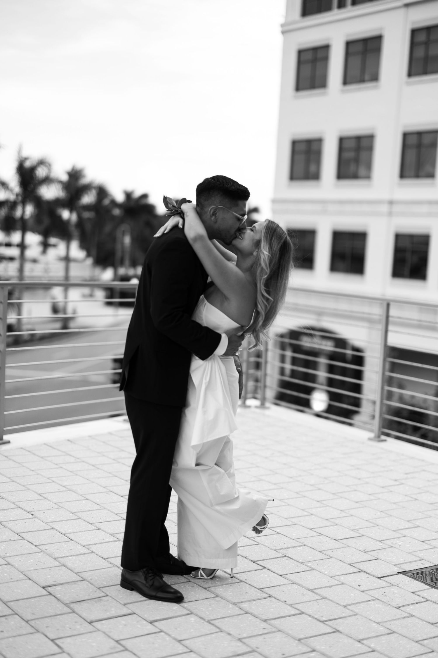 A romantic black and white wedding photo series showing a couple embracing on a modern balcony.