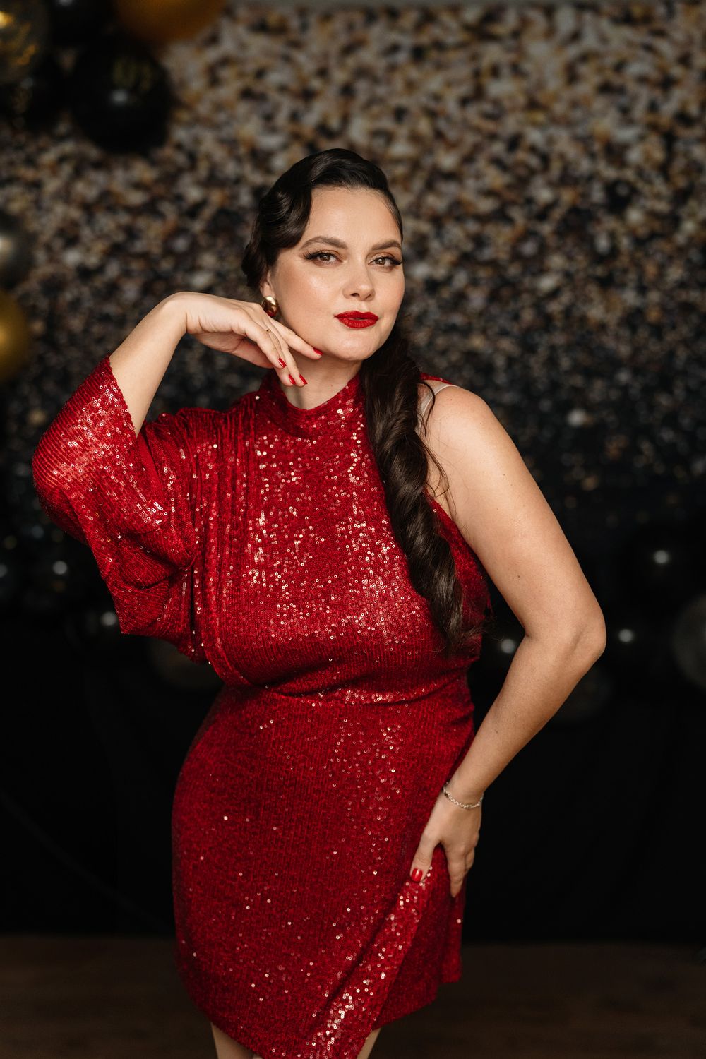 A person poses in a sparkly red sequined dress against a dark background with glittering bokeh effects.