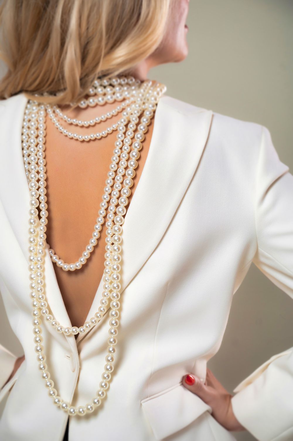 Elegant white blazer adorned with layered pearl necklaces draping down an open back.