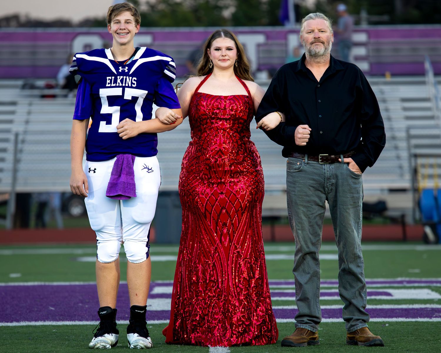 A person in a red sparkly dress poses with football players on a field during what appears to be a game day celebration.