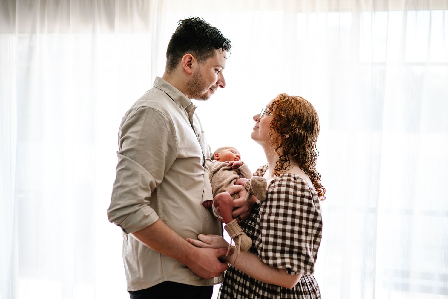 A happy family shares tender moments together with white backdrop taken during an in-home newborn photo session in Melbourne.
