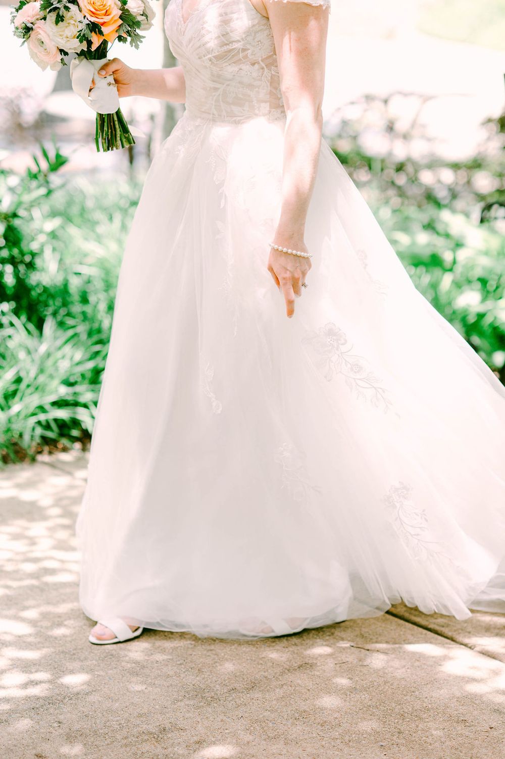 Three detail shots of a flowing white wedding dress with delicate lace details as it sweeps across a stone pathway.