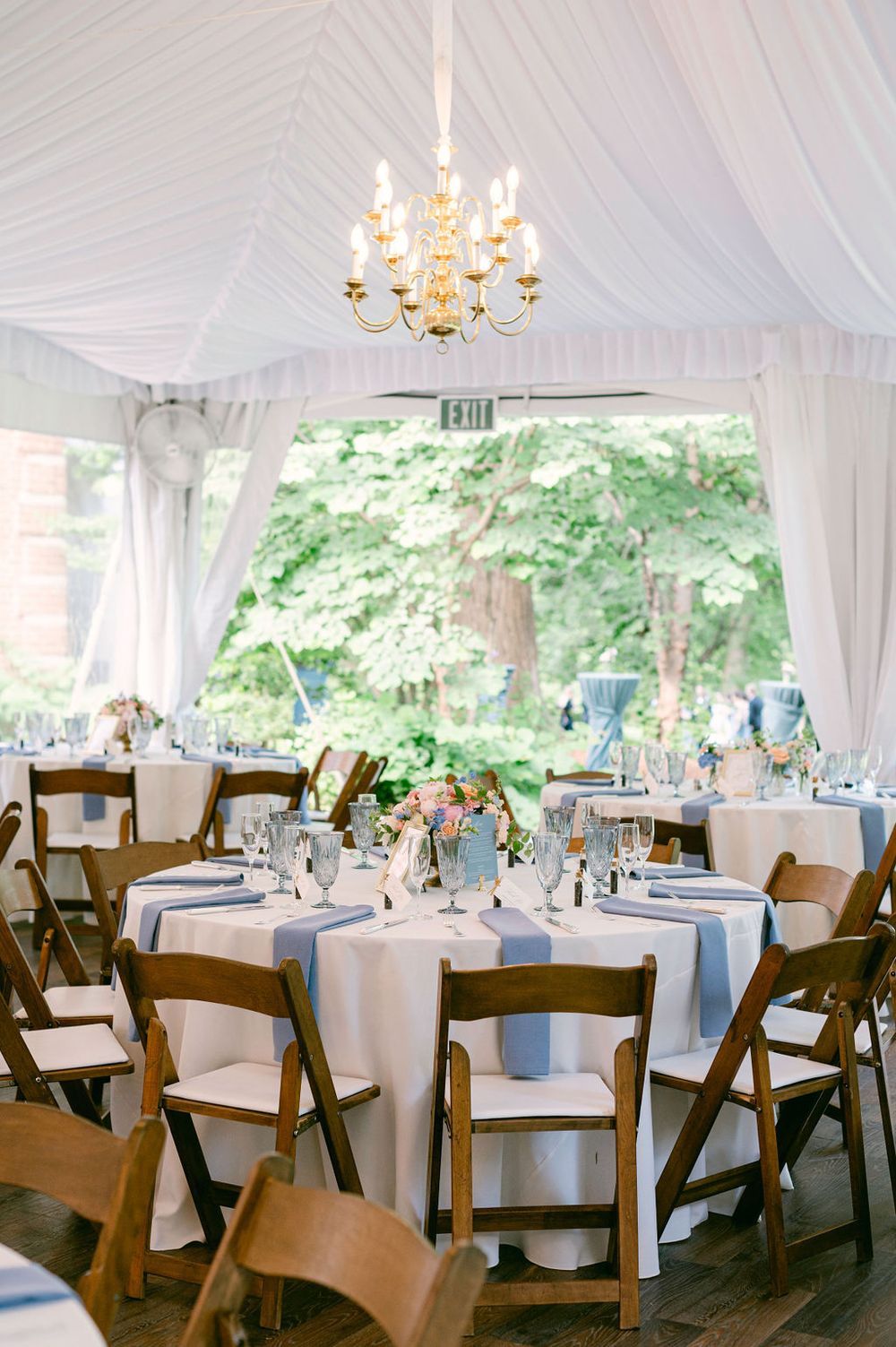 Elegant wedding reception tent with white draping, crystal chandeliers, round tables and dark wooden chairs.