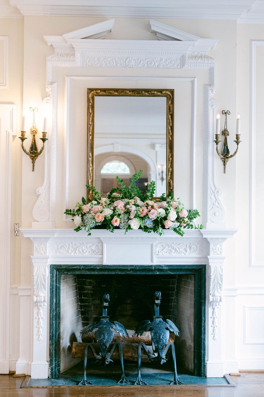 Elegant white fireplace mantels adorned with floral arrangements and candle sconces in a formal room.