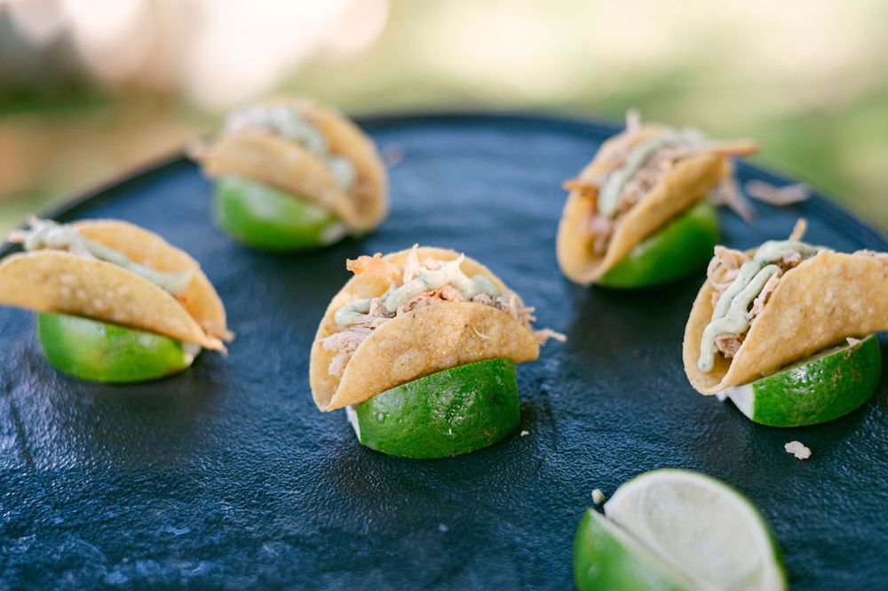 Fresh tacos arranged on a dark slate surface with lime wedges and garnishes.