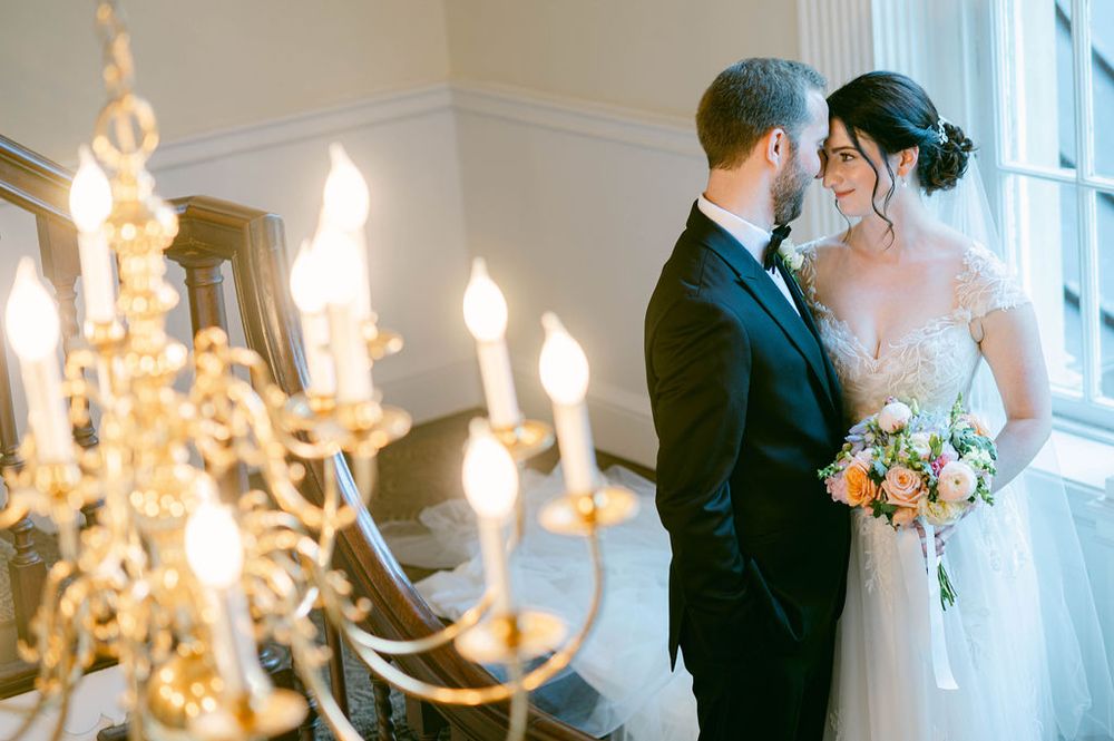 A romantic moment between newlyweds by a window with an elegant crystal chandelier in the background.