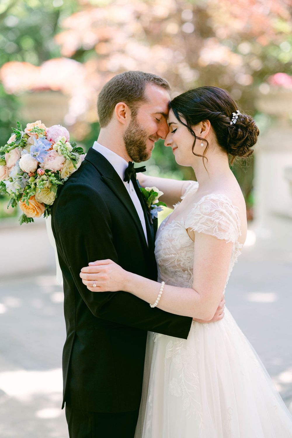 A romantic wedding couple embraces outdoors under soft spring lighting with delicate floral arrangements.