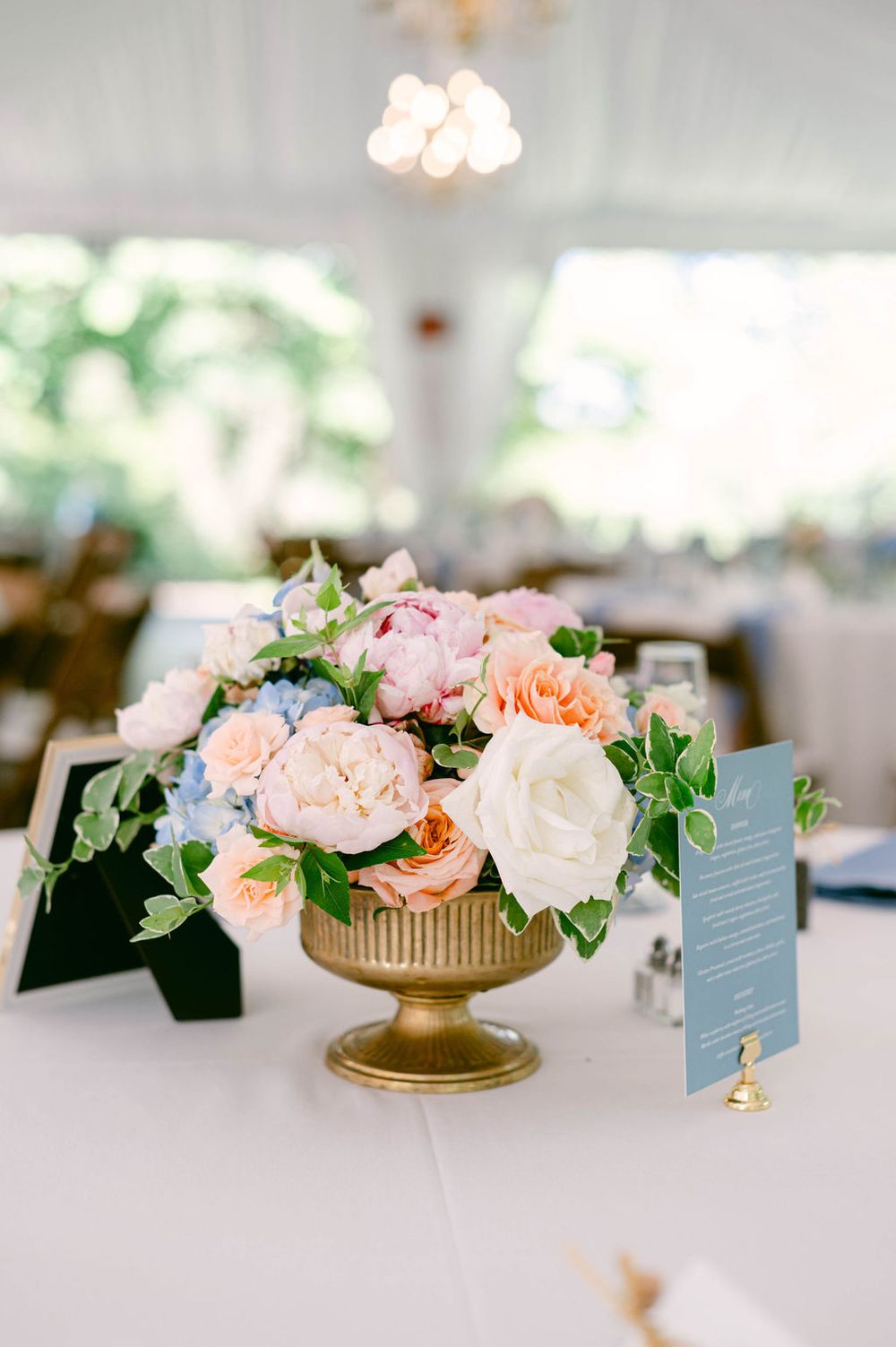 Elegant wedding table centerpieces featuring blush pink and peach roses in gold pedestal vases with table numbers.