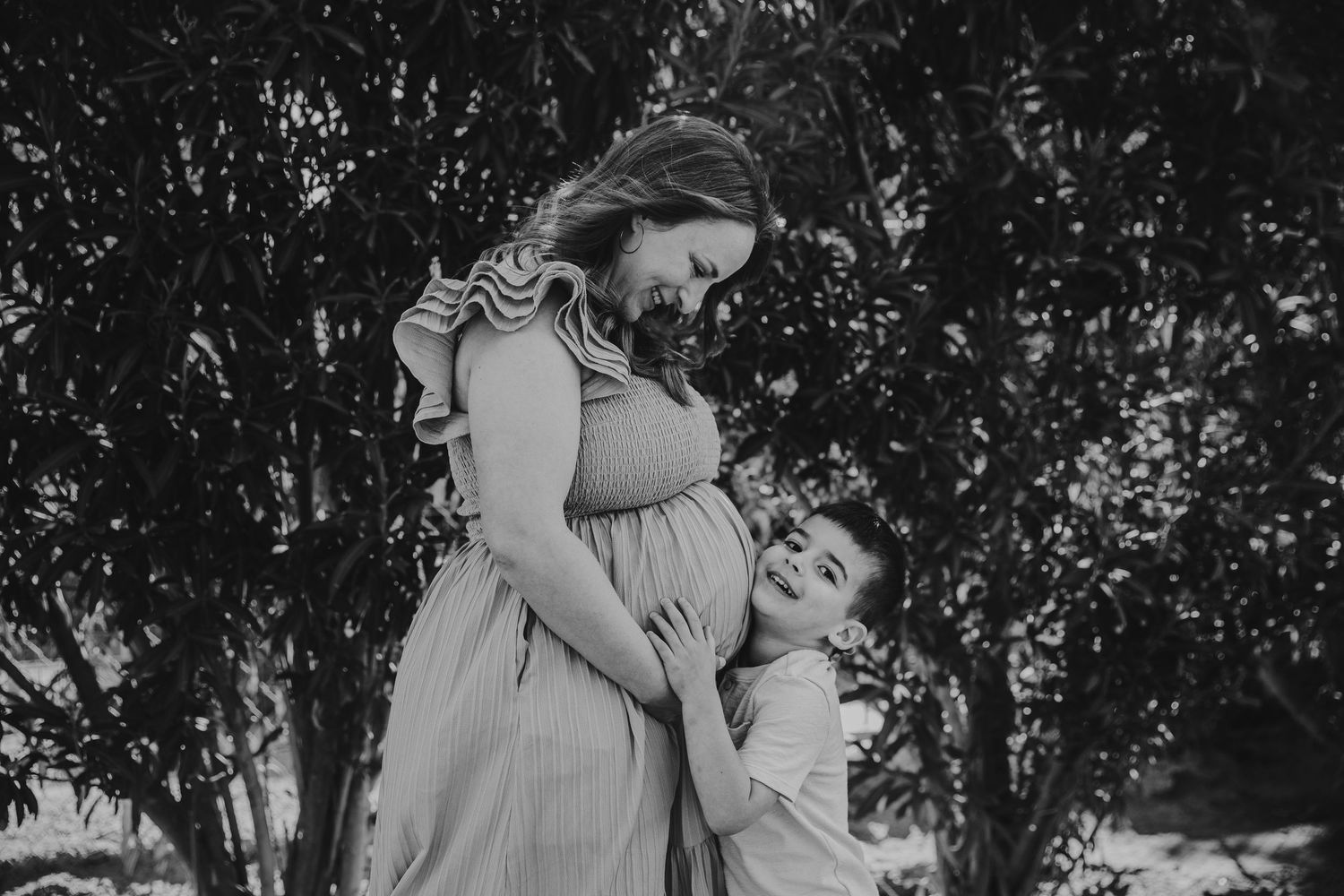 Black and white portrait of a tender family moment under tree branches.
