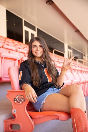 Person relaxing in casual attire on orange stadium seats at a sports venue.