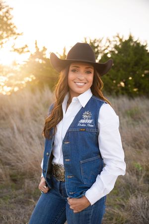 A person wearing a denim vest and white shirt poses in a field during golden hour sunset.