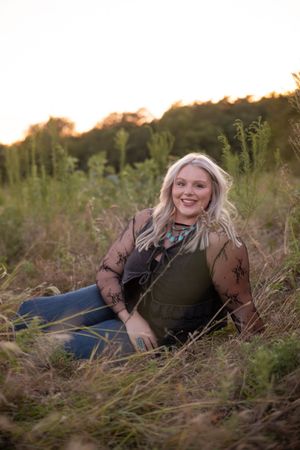 A person in casual attire poses playfully in tall grass during golden hour sunset.