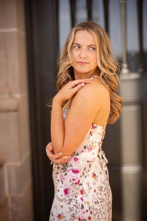 Woman in floral dress poses against architectural columns in warm evening light.