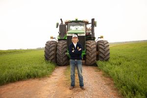 A person stands between two large agricultural tractors on a dirt road surrounded by green fields.