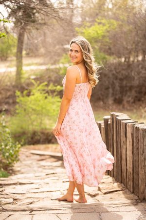 A series of photos showing someone in a flowing pink floral dress walking along a rustic wooden fence in sunlit nature.