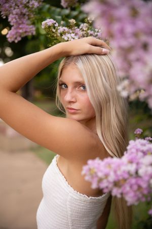 A woman in a white top poses gracefully near blooming pink cherry blossoms in a springtime portrait series.
